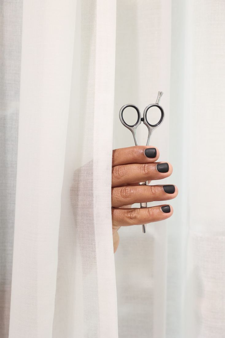 A stylist holding scissors behind a sheer white curtain
